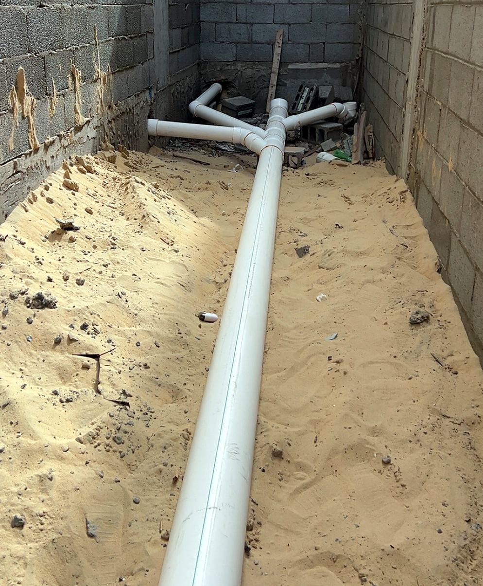 A white drain line laid in sand with branches at its end, before backfilling