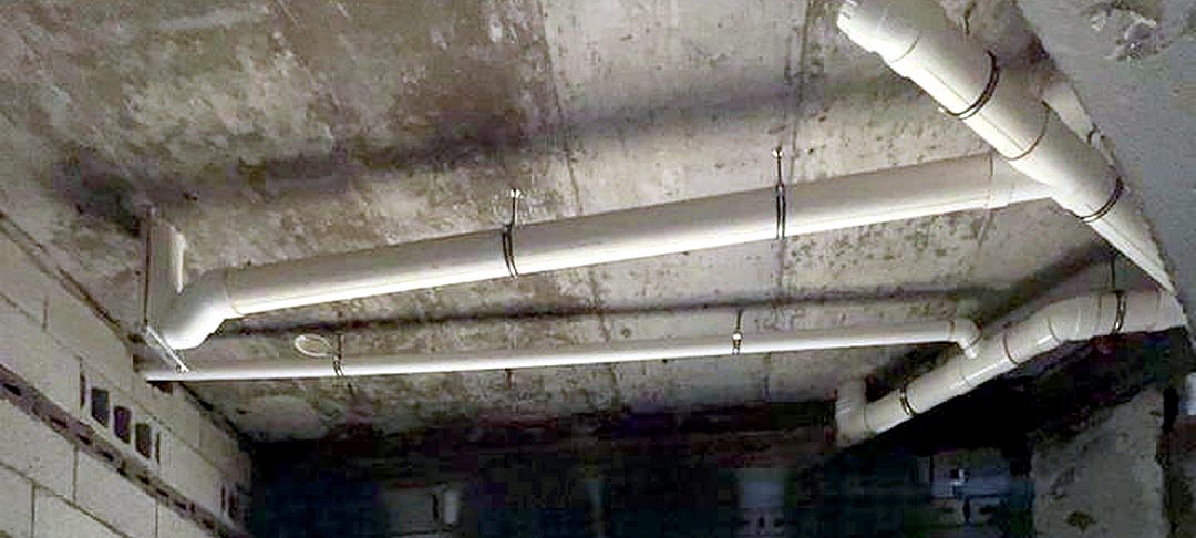 White drain pipes hung with clamps under a concrete ceiling