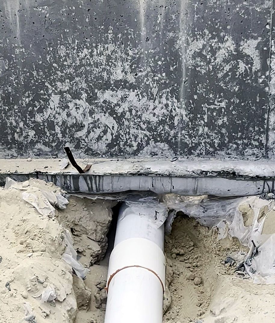 A white drain pipe passing under a concrete beam