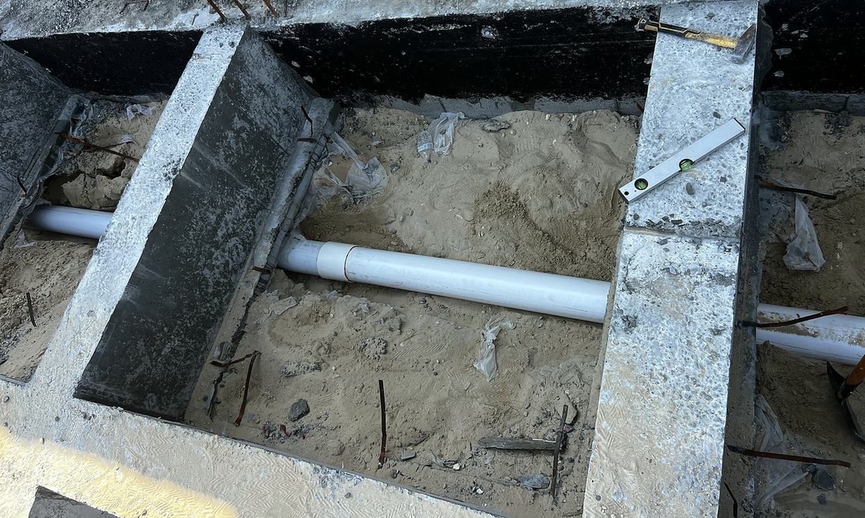 A white drain pipe inside a concrete section with a level on its edge