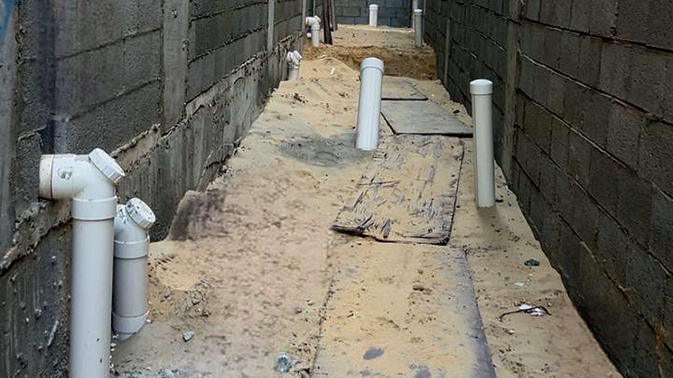 A side passage of a building under construction with white drain and vent risers over sand